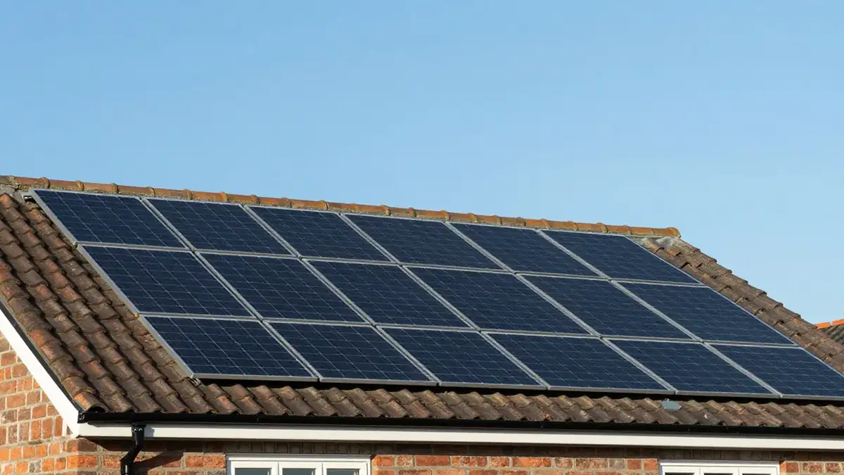Two rows of black solar panels covering a tiled roof slope against a clear blue sky